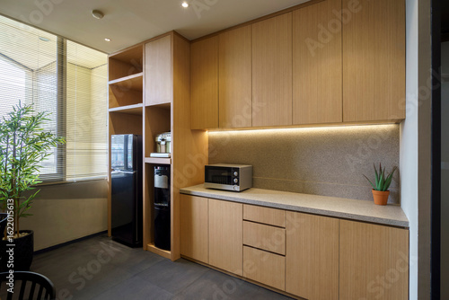 Modern office pantry with wooden cabinets, microwave, and water dispenser. A minimalist and functional kitchen area for a contemporary workspace.