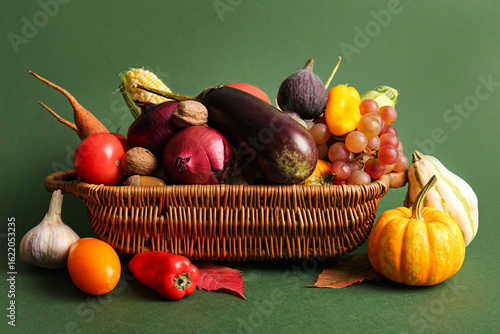 Fototapeta Naklejka Na Ścianę i Meble -  Wicker basket with fresh vegetables, fruits and autumn leaves on green background. Harvest festival