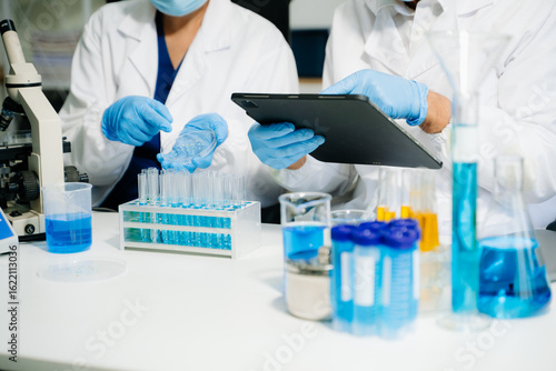 Fototapeta Scientists in a clean lab environment analyzing samples using test tubes and a tablet, showcasing modern biotech research, diagnostics, and medical innovation