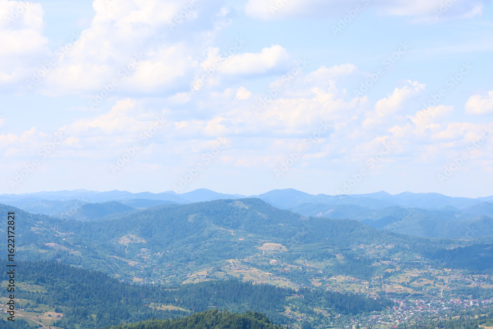 Obraz premium A massive mountain range, covered with dense forests, stretches to the horizon, where it dissipates into a light haze. The image illustrates the majesty, tranquility, and natural beauty of the mountai