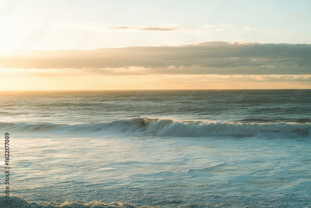 Obraz premium Sunlight reflects off gentle waves as the vibrant orange sky of a sunset paints the horizon over a sandy beach