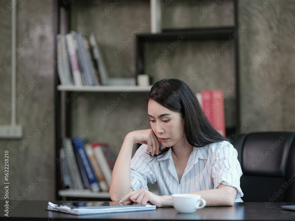 An Asian woman sitting at home, working on a digital tablet, feeling stressed and tired, in a business setting. An Asian woman sitting at home, working on a digital tablet, feeling stressed and tired, in a business setting.