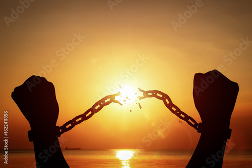 Silhouette of raised hands breaking chains on sunset background. Concept of fight for freedom, and overcoming limitations.