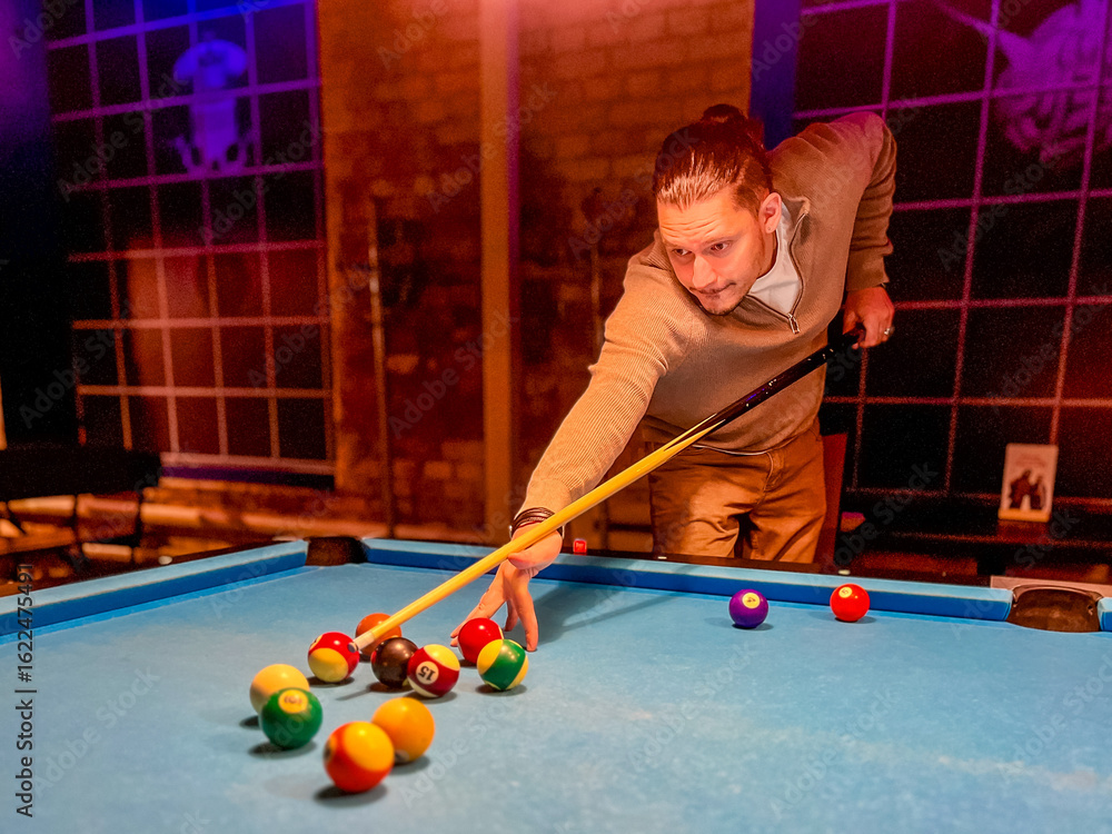 Fototapeta premium Brunette middle-age man holding arm on billiard table, playing snooker game or preparing aiming to shoot pool balls. sport game snooker billiards