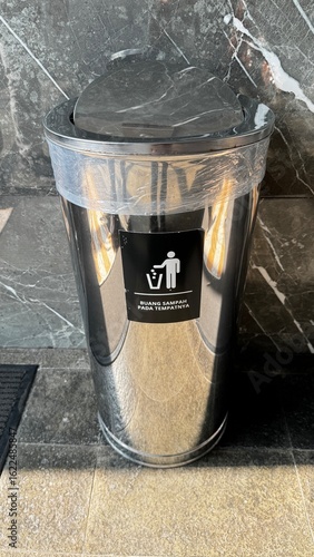 A modern, stainless steel trash can with a marble-like lid and an Indonesian 