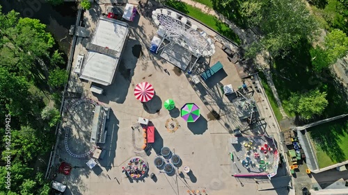Top-down drone video showing a colorful amusement park installation at City Park Ice Rink & Boating in Budapest. Calm morning scene with vibrant rides and green surroundings.