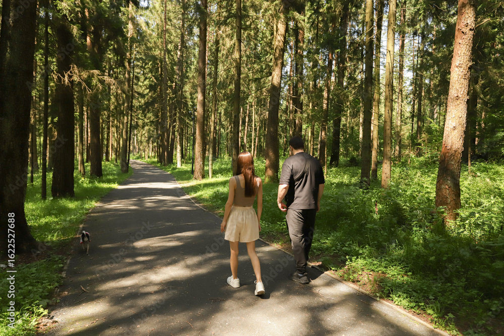 Fototapeta premium Pet owners walking with their small dog through a green forest trail, symbolic of modern life balance, pet love, and connection to nature
