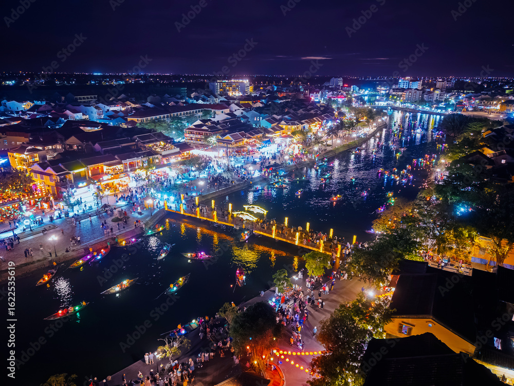 Fototapeta premium Bustling night market and lantern festival along Hoi An, Vietnam. Landmark bridge with river and boats with tourist