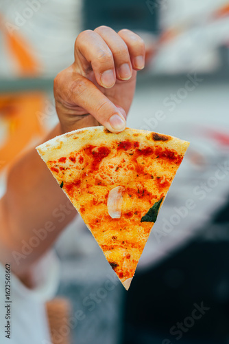 Close-up of a person picking up a slice of freshly baked pizza with melted cheese, ham, and tomato sauce from a metal plate. Perfect moment capturing gooey cheese stretch and delicious detail.