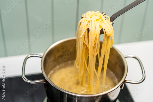 Long spaghetti strands soften as they boil bubbling water. Spaghetti cooks in a pot of hot water to perfectly al dente. Spaghetti swirling in boiling water preparing a delicious pasta