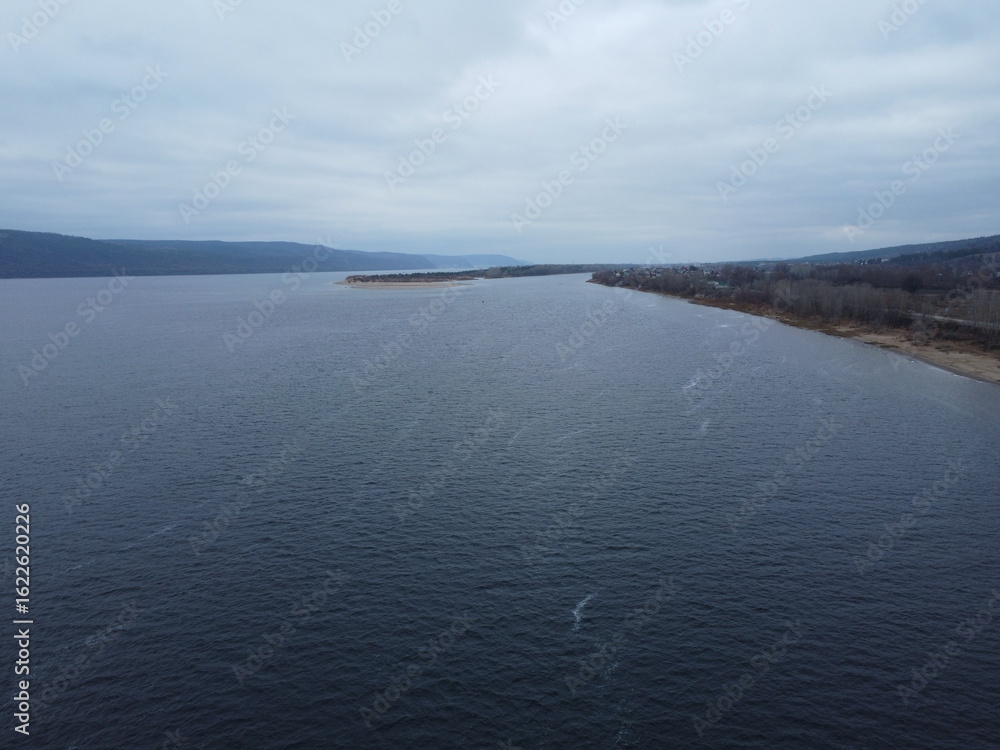 Fototapeta premium Tranquil Waterscape: A serene body of water under an overcast sky, inviting contemplation. The natural tones and textures convey a feeling of peacefulness and vastness.