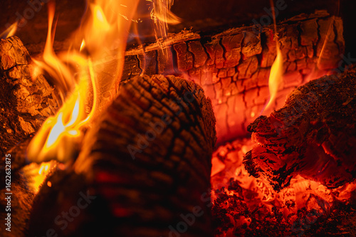 Cozy background of burning logs in a fireplace. Close-up of glowing embers and warm flames. Concept of comfort, warmth, and winter hygge