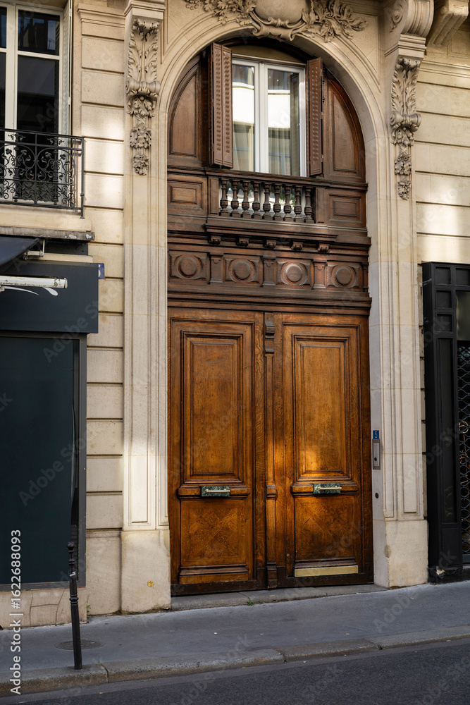 Naklejka premium Elegant Parisian Building Entrance: Ornate Wooden Double Doors, Architectural Detail, Warm Sunlight