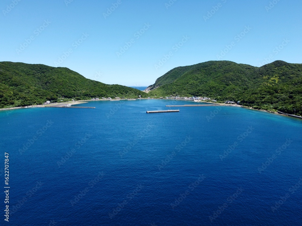 Obraz premium Crystal clear waters and rocky beach at Ikezuka, Naru Island, Goto Islands, Nagasaki, Japan – stunning summer coastline with lush green hills and transparent turquoise sea.