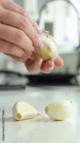 Extreme close-up video of a clean human hand meticulously peeling a pristine garlic clove, revealing its smooth inner surface on a stark white kitchen counter, bathed in natural daylight, capturing