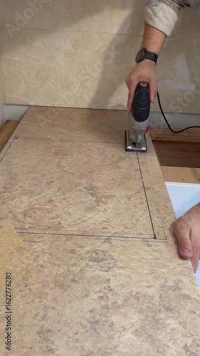A person's hands using an electric jigsaw to cut a kitchen countertop. A concept of home renovation, DIY, and professional craftsmanship.