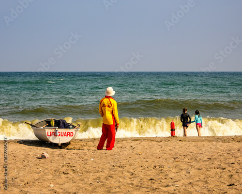 Canvas Print lifeguard with row boat and safety equipment watching children playing on the be