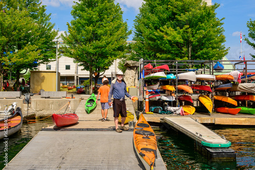 Wallpaper Mural healthy active senior lifestyle: man (sun hat, sun glasses, grey beard,) cleaning a sea kayak on a busy colorful dock on toronto harbour in summer Torontodigital.ca