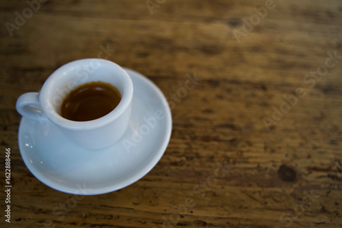 Blurred photo of Espresso coffee in a white cup on a rustic wooden table with natural light creating a warm ambiance. Copy space