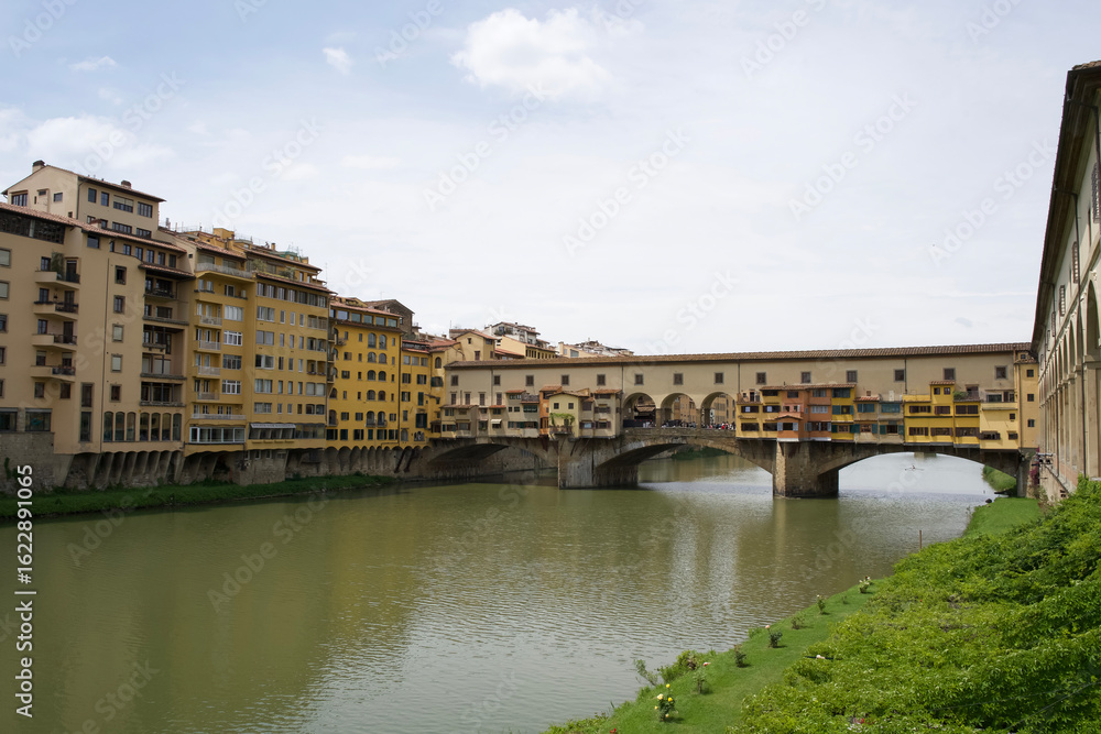 Obraz premium Ponte Vecchio bridge in Florence, Italy with colorful buildings along the riverbank and clear blue sky above