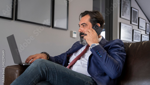 Фотография A middle-aged, dark-haired businessman in a suit is sitting on a leather couch i