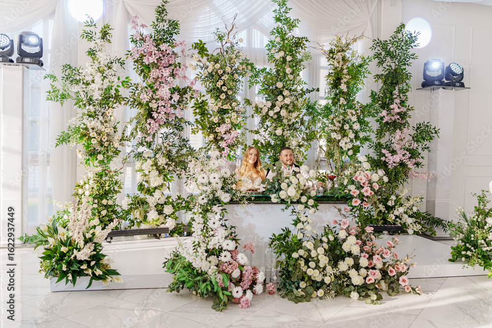 Fototapeta premium The bride and groom at the newlyweds' table, decorated with many flowers.