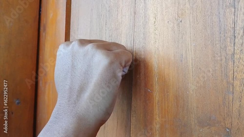 Portrait of a woman's hand knocking on the wooden door of a house.