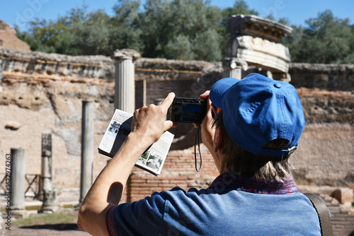 Tableau sur toile Tourist photographing ancient ruins with camera and guidebook in hand