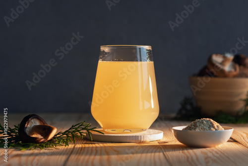 Fotografie Golden adaptogenic mushroom elixir glows in a modern glass on rustic wood, surrounded by powder and shiitake, radiating natural wellness