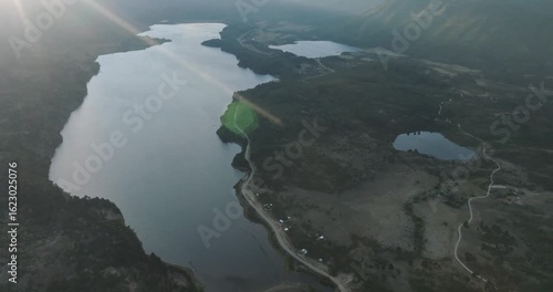 Sun rays pierce clouds over lake and smaller bodies of water surrounded by forested mountains in Patagonia under a partly cloudy sky