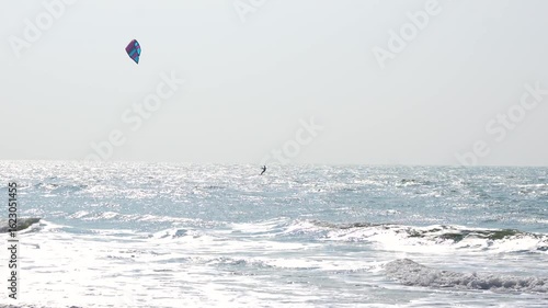 Kite surfer riding waves on sunny day with sparkling ocean water and clear sky