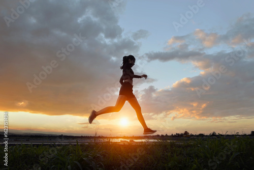 Full length side view of a young woman jogging through a rural landscape at sunset, Thailand