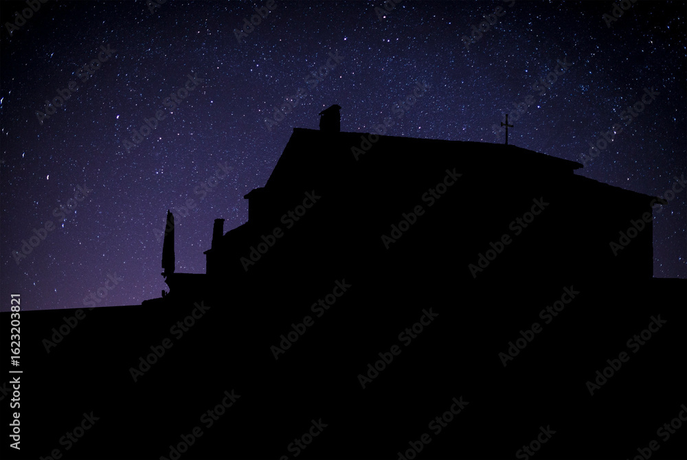 Obraz premium Silueta de una iglesia o edificio con una cruz en el techo, destacando contra un cielo estrellado. Imagen simbólica que evoca espiritualidad, reflexión y conexión con lo divino.