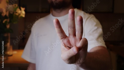 Man's hand displaying three fingers in a dimly lit room. Showing crown or trident with fingers