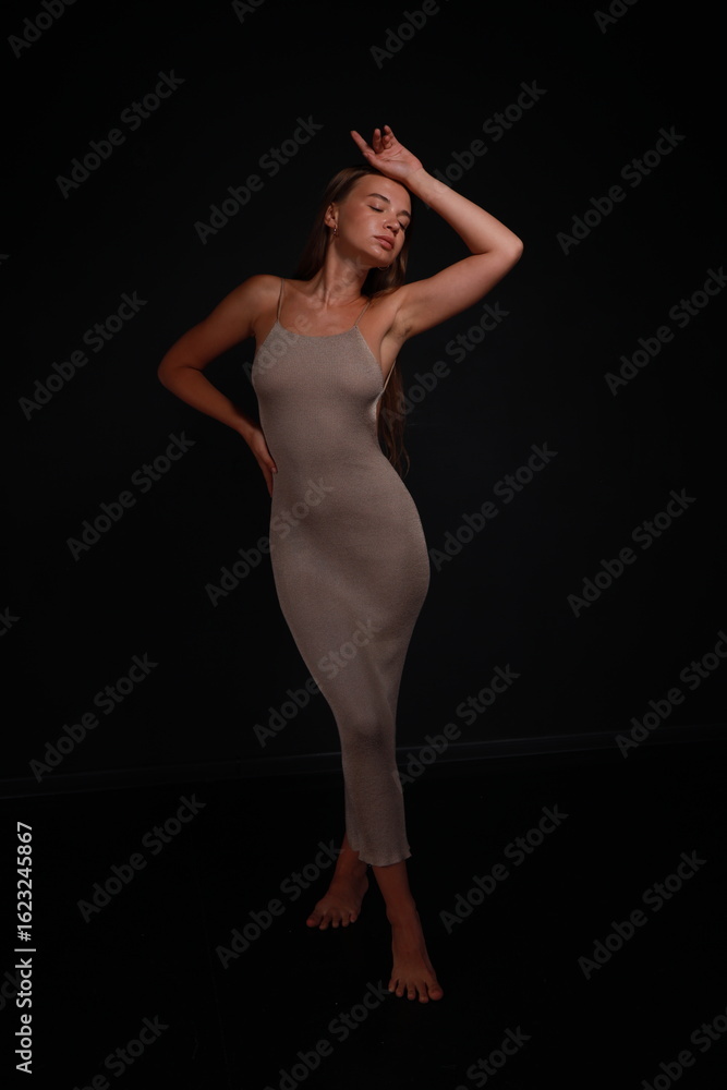 Naklejka premium Slender barefoot young woman in grey dress full length low key portrait