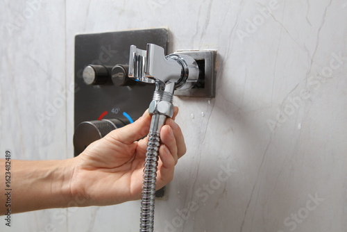 Photography A person's hand is shown inserting a chrome shower hose into a square wall mount