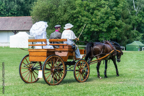 Horse-drawn carriage with coachman and passengers dressed in elegant interwar-era style outfits.