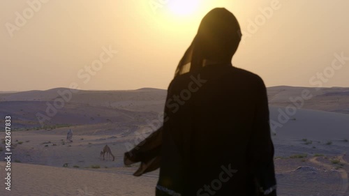 Arabic woman lady with Abaya cloth slow motion standing looking at the sun in the desert sand dune sunset