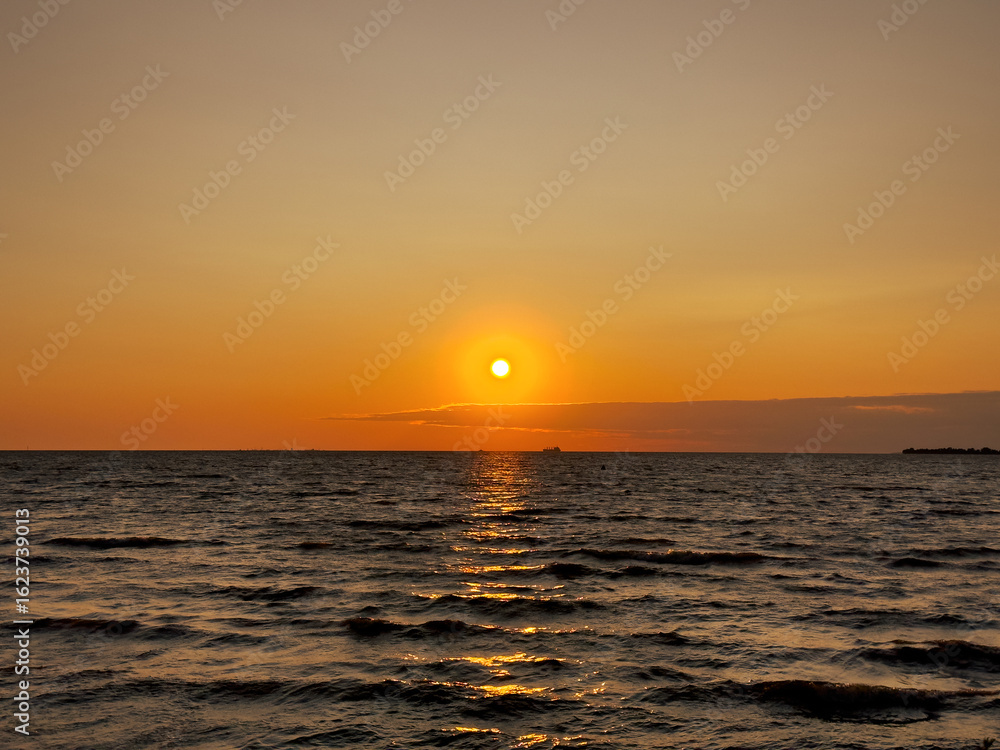 Obraz premium Beautiful sunset over the sea. The sun sets on the water. The sky is painted with bright colors. Summer evening. Sunset beach