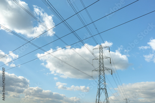 Electricity pylon or tower with power lines running across a blue sky with clouds
