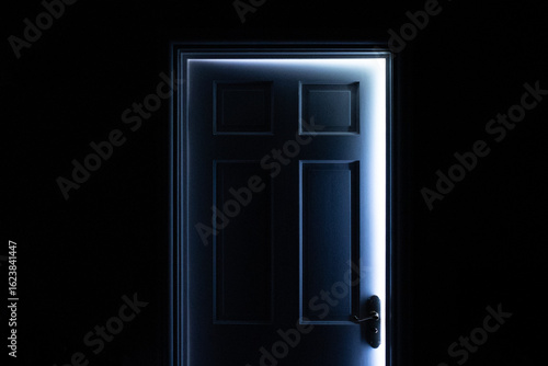 Slightly open or ajar door letting in daylight against a totally black foreground with space for text or copy