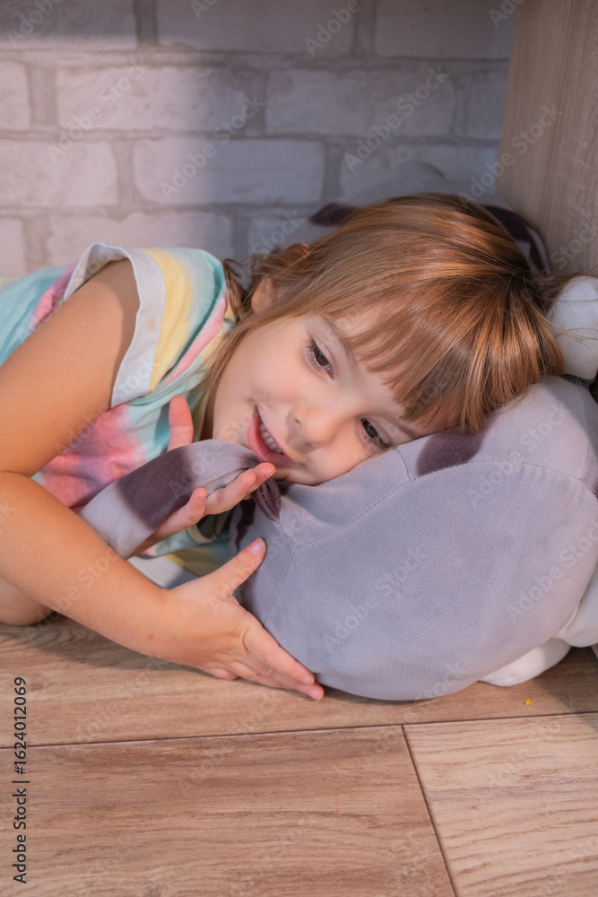 Naklejka premium young girl lies on the floor, resting her head on a plush toy