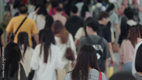 Bangkok walkway filled with diverse individuals commuting in an urban setting. A blend of clothing styles, direction, and movement captured from behind. Daytime scene, high energy