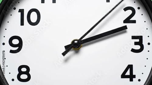A close-up video of an analog clock. The clock face is white with black numbers and hands. The video focuses on the movement of the second hand, which sweeps continuously.