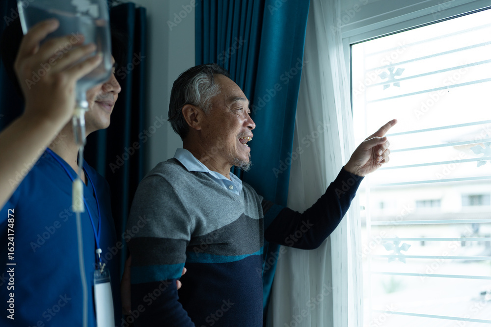 Fototapeta premium senior man patient standing near window looks outside with his elderly nurse assistant. home caregiver nurse visit retirement patient for health check up recovery process medical service
