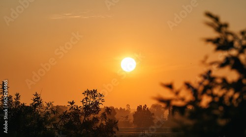 Fiery orange sunset sky with round sun above hazy horizon in peaceful setting