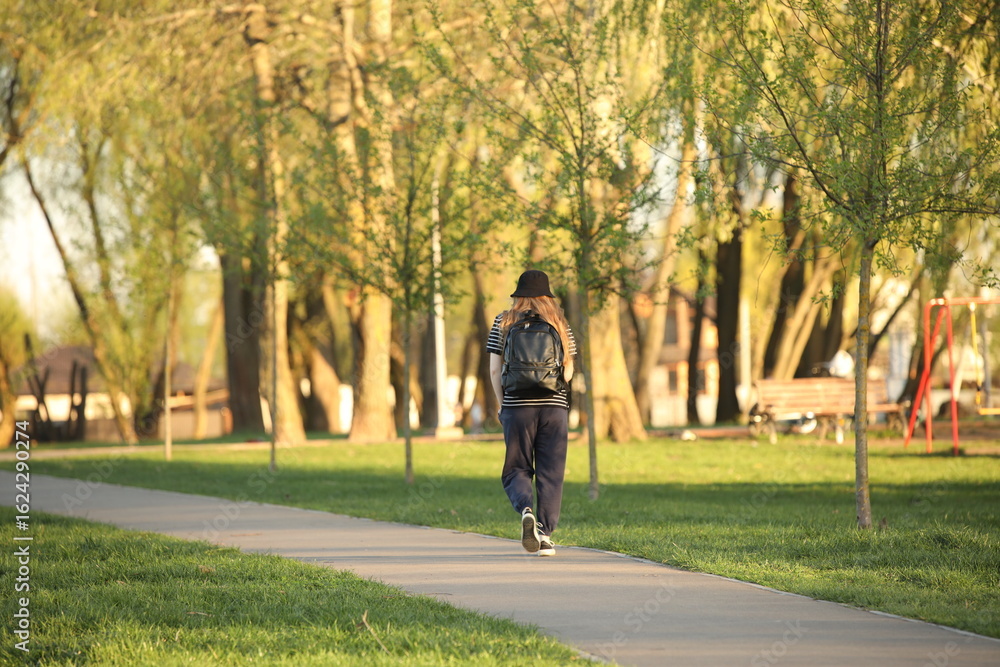A young girl in a sports uniform walks alone along a park alley. A walk in the fresh air among summer greenery. Fashion of modern youth. A young girl in a sports uniform walks alone along a park alley. A walk in the fresh air among summer greenery. Fashion of modern youth.