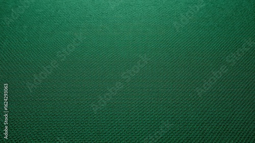Close up view of an emerald green textile with a repeating diagonal pattern in a dark environment