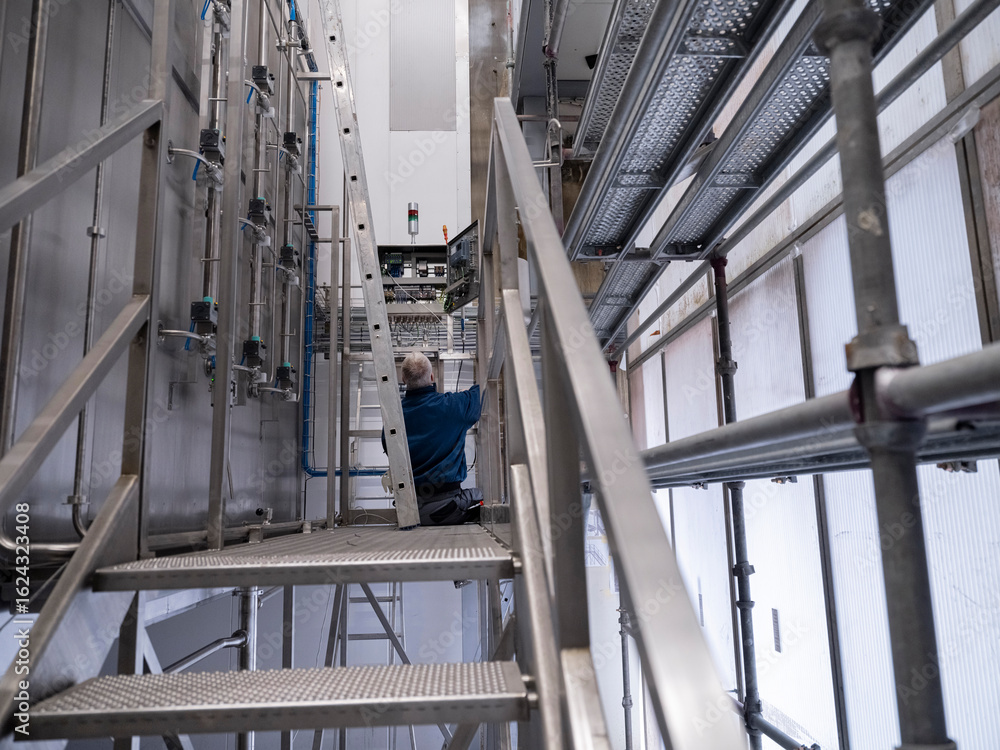 Fototapeta premium Worker on elevated platform performing maintenance work on industrial equipment in manufacturing facility