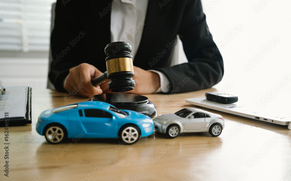 Fototapeta premium A lawyer uses a gavel near a toy car, symbolizing legal proceedings, car insurance claims, court decisions, accidents, liability, and justice in automotive-related legal cases.